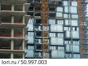Concrete highrise building under construction, with crane and prefabricated modules, design for urban planning, architecture, and infrastructure projects. Стоковое фото, фотограф Данила Большаков / Фотобанк Лори