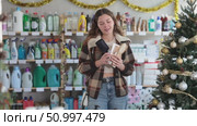 Happy young female buyer choosing convenient comb in large store with New Year decoration. Стоковое видео, видеограф Яков Филимонов / Фотобанк Лори