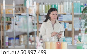 Attentive middle-aged female client scrolling phone while looking for something in drugstore. Стоковое видео, видеограф Яков Филимонов / Фотобанк Лори