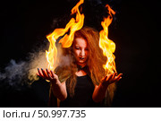 An ominous witch with long curly hair holds a magical fire. Tongues of flame on the palms of a red-haired smirking woman. Witchcraft. Стоковое фото, фотограф Михаил Решетников / Фотобанк Лори
