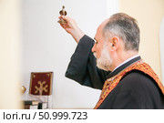 Russia, Rostov-on-Don - May 30, 2014: An Armenian priest holds a bird figurine in his hand and performs the rite of baptism over the font. Редакционное фото, фотограф Екатерина Красникова / Фотобанк Лори