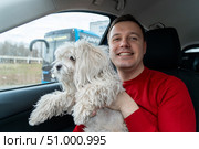 Happy man hugs his white lapdog and smiles at camera. Owner of a fluffy Chinese crested dog travels by car. Travel with pet concept. Стоковое фото, фотограф Данила Большаков / Фотобанк Лори