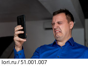 Caucasian man crying while looking at text message in cellphone. heartbroken millennial man looks at screen of smartphone and grieves. Tragedy in the family. Concept of Feeling Stressed, Anxiety. Стоковое фото, фотограф Данила Большаков / Фотобанк Лори