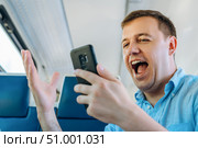 Overjoyed caucasian man looks at smartphone screen with mouth opened in train commuting to work. Excited man looking with wide open eyes into smartphone being shocked by what he sees on way to work. Стоковое фото, фотограф Данила Большаков / Фотобанк Лори