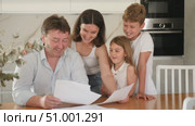 Happy satisfied family reading documents together while sitting at the table at home. Стоковое видео, видеограф Яков Филимонов / Фотобанк Лори