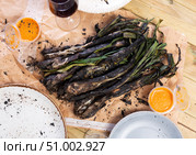 On wooden table covered with paper, fried Catalan green onion kalsot and two small balls of sauce. Стоковое фото, фотограф Яков Филимонов / Фотобанк Лори