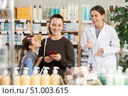 Happy mother with daughter scrolling phone while looking for something in drugstore. Стоковое фото, фотограф Яков Филимонов / Фотобанк Лори