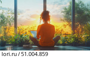 A person is sitting cross-legged on the floor, using a laptop while enjoying the calming sunset view through large windows filled with plants. Стоковое AI-видео, аниматор Данила Большаков / Фотобанк Лори