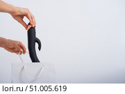 A woman makes a purchase and puts a dildo in a bag on a white background. Close-up of female hands with a black vibrator. Стоковое фото, фотограф Михаил Решетников / Фотобанк Лори