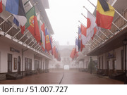 SOCHI, RUSSIA - MAY 03, 2024: A man walks through the Olympic village, Olympic village with a view of buildings and national flags of different countries on a foggy spring day. Редакционное фото, фотограф Наталья Угрюмова / Фотобанк Лори