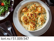 Cauliflower creamy soup with baked cauliflower florets on the top in a white bowl on a dark wood tabletop. Restaurant style dish. Hot, delicious plate of cream-of-cauliflower soup with melted cheese. Стоковое AI-изображение, AI-художник Марина Демидюк / Фотобанк Лори