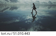 Lonely figure walking on reflective surface under cloudy sky at coastal location during sunset. Стоковое AI-видео, аниматор Сергей Толмачёв / Фотобанк Лори