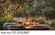 A beautifully arranged outdoor table is set for a romantic dinner, surrounded by twinkling lights and nature's serenity during sunset. Стоковое AI-видео, аниматор Данила Большаков / Фотобанк Лори