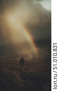 Man walks along a trail under a vibrant rainbow amidst cloudy skies in a dramatic landscape setting. Стоковое AI-видео, аниматор Сергей Толмачёв / Фотобанк Лори