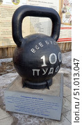 100 пудовая чугунная  гиря копилка в городе Верхнеуральск Челябинская область на фоне баннера о истории вернеуральского уезда на фасаде здания краеведческого музея. Редакционное фото, фотограф Надежда Бирюкова / Фотобанк Лори