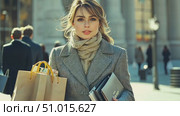 A stylish woman in a coat holds shopping bags and a laptop while navigating a lively urban street bustling with people in the afternoon. Стоковое AI-видео, аниматор Данила Большаков / Фотобанк Лори