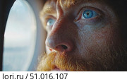 A man with striking blue eyes stares pensively out of an airplane window, immersed in thought as the morning light shines through. Стоковое AI-видео, аниматор Данила Большаков / Фотобанк Лори