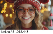 A young woman with glasses beams joyfully while wearing a festive hat and sweater, surrounded by warm holiday lights in a cheerful atmosphere. Стоковое AI-видео, аниматор Данила Большаков / Фотобанк Лори