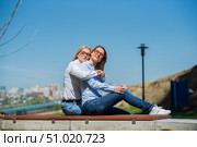 Two surprisingly similar women are sitting on a bench in an embrace and smiling. A middle-aged woman and her elderly mother. Beautiful well-groomed mother and daughter family look. Стоковое фото, фотограф Михаил Решетников / Фотобанк Лори