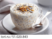 Healthy overnight oats with seeds and milk served in a glass cup. Стоковое AI-изображение, AI-художник Катерина Бондарец / Фотобанк Лори