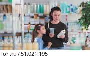 Woman stands in a European pharmacy with her daughter and chooses a foot cream and body lotion. Buying high-quality care cosmetics in a pharmacy. Стоковое видео, видеограф Яков Филимонов / Фотобанк Лори