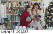 Tech-savvy teenage girl scanning bottle of glass cleaner with smartphone while shopping with mother in household goods store decorated for Christmas, using mobile payment app for cashless transaction. Стоковое видео, видеограф Яков Филимонов / Фотобанк Лори