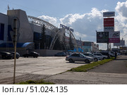 Magnitogorsk, Russian Federation - August 05, 2025: Gostiny Dvor shopping center entrance with modern architecture and blue glass facade, surrounded by trees and parked cars, showcasing urban lifestyle. Редакционное фото, фотограф Ирина Ручушкина / Фотобанк Лори