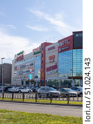 Magnitogorsk, Russian Federation - August 05, 2025: Modern shopping center with large glass facade and vibrant signage, showcasing various brands and stores in a bustling urban environment. Редакционное фото, фотограф Ирина Ручушкина / Фотобанк Лори