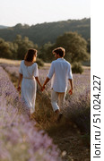 Couple strolls hand in hand through a lavender field during sunset in warm golden light. Стоковое AI-изображение, AI-художник Сергей Толмачёв / Фотобанк Лори