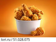 Crispy chicken on a yellow orange color background. Bucket overflowing with golden Fried Chicken Strips. Street food. Coated batter southern style chicken drumsticks and pieces. BBQ Feast. Nuggets. Стоковое AI-изображение, AI-художник Марина Демидюк / Фотобанк Лори