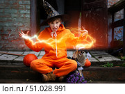A child in an orange costume and a wizard hat for Halloween. The boy holds the skeleton and conjures a magical magical lightning bolt. Стоковое фото, фотограф Лазаренко Светлана / Фотобанк Лори