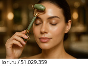Close-up of serene woman with eyes closed using a jade roller on her forehead for skincare and relaxation in soft lighting. Стоковое AI-изображение, AI-художник Башкирова Анна / Фотобанк Лори