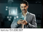 Professional man analyzes financial data on smartphone in a modern office environment during the workday. Стоковое фото, фотограф Сергей Толмачёв / Фотобанк Лори