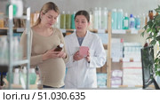 Pregnant woman choosing medicinal syrup with help of young female pharmacist at pharmacy. Стоковое видео, видеограф Яков Филимонов / Фотобанк Лори
