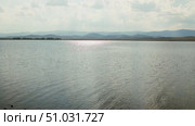 Bashkortostan, Russian Federation - August 07, 2025: Serene lake view reflecting sunlight with distant mountains under a cloudy sky, creating a tranquil natural landscape for relaxation and inspiration. Редакционное видео, видеограф Ирина Ручушкина / Фотобанк Лори
