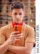 Young man with headphones looking at smartphone outdoors in urban setting. Стоковое фото, фотограф Raquel Corcoles Mendez / Фотобанк Лори
