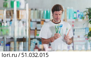 Adult man stands in a European pharmacy and chooses a set of dental care on the recommendation of the dentist. Purchase of dental hygiene products. Стоковое видео, видеограф Яков Филимонов / Фотобанк Лори