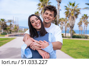 Happy young couple hugging and smiling on palm-lined seaside promenade. Стоковое фото, фотограф Raquel Corcoles Mendez / Фотобанк Лори