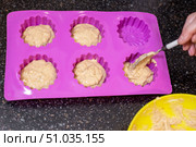 A hand carefully spoons batter into a silicone baking pan, preparing individual servings of banana muffins. Стоковое фото, фотограф Коханова Наталья / Фотобанк Лори