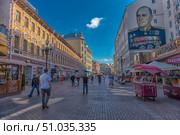 A pedestrian street in Moscow with bright historical building facades, cozy cafes and shops. On the wall of one of the houses there is a large graffiti with a portrait of Marshal Georgy Zhukov in a ceremonial uniform with orders and medals. Strollers, blue sky and sunlight create the atmosphere of a promenade and tourist center of the city. (2018 год). Редакционное фото, фотограф Анна Кривицкая / Фотобанк Лори