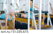 Positive mature woman practicing pilates stretching exercises on reformer at gym. Стоковое видео, видеограф Яков Филимонов / Фотобанк Лори
