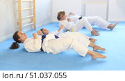 Concentrated tweens with parents in traditional martial arts attire participating in intense training session, practicing abdominal crunches combined with hand strikes. Стоковое видео, видеограф Яков Филимонов / Фотобанк Лори