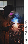 A skilled welder in protective gear carefully fuses metal with a welding torch, creating a dazzling display of sparks and bright blue flames in a dimly lit workshop. Стоковое AI-видео, аниматор Владимир Федоров / Фотобанк Лори