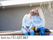 Two surprisingly similar women are sitting on a bench in an embrace and smiling. A middle-aged woman and her elderly mother. Beautiful well-groomed mother and daughter family look. Стоковое фото, фотограф Михаил Решетников / Фотобанк Лори