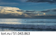 Morning by the ocean. The clouds in the sky are illuminated with golden light. The waves are foaming on the beach. The head of a swimming man is visible in the distance. Malaysia. Borneo.Kota Kinabalu. Стоковое фото, фотограф Вера Ивановна Кубарева / Фотобанк Лори