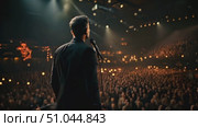 A man stands confidently in front of a microphone addressing a large crowd. The audience attentively listens as he delivers a speech. Стоковое AI-видео, аниматор Данила Большаков / Фотобанк Лори