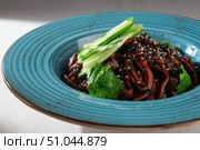 Traditional Korean jajangmyeon noodles with rich black bean sauce, fresh cucumber, sesame seeds and herbs served in a rustic blue ceramic bowl. Стоковое фото, фотограф Aleksandr Gavrilychev / Фотобанк Лори