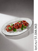Crispy fried chicken wings coated in a rich Korean yangnyeom sauce, served on a white plate and garnished with sesame seeds and fresh cilantro. Стоковое фото, фотограф Aleksandr Gavrilychev / Фотобанк Лори