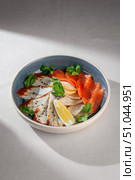 Gourmet selection of sliced seafood including smoked salmon, marinated fish fillet and calamari, garnished with sesame seeds, lemon wedge and fresh parsley in ceramic bowl. Стоковое фото, фотограф Aleksandr Gavrilychev / Фотобанк Лори
