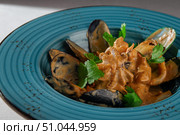 Cooked mussels in shells served with a rich spicy creamy sauce and fresh herbs in a rustic blue bowl on a light tablecloth, top-down view. Стоковое фото, фотограф Aleksandr Gavrilychev / Фотобанк Лори